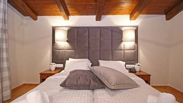 Una cama doble con cabecera capitonada, dos mesitas de noche con lámparas, y techo de madera.
