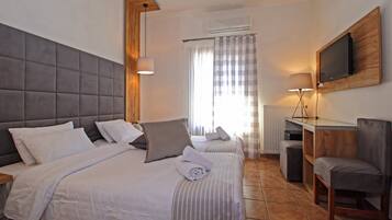 Habitación de hotel con una cama grande, un escritorio con silla, un televisor montado en la pared y una ventana con cortinas.