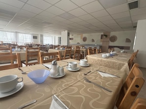 A dining area with multiple tables set for breakfast, each with plates, cups, and cutlery.