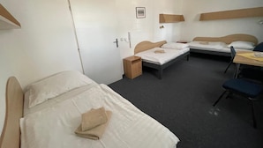Habitación de hotel con dos camas individuales, un escritorio, una silla, una mesita y una puerta.