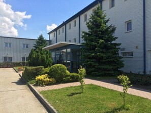 En byggnad med en överbyggd entré, en gräsmatta och ett stort, vintergrönt träd.