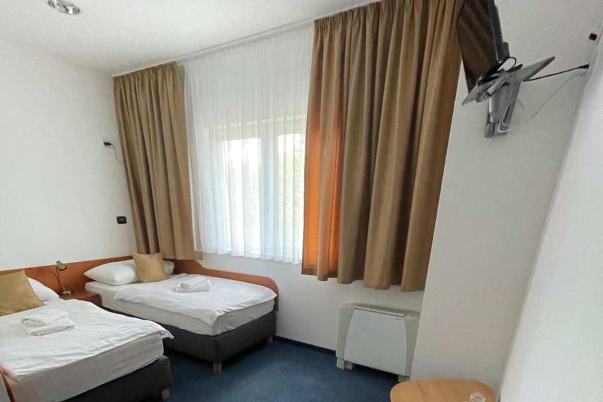 A hotel room with two beds, a desk, a chair, a television, and a window with curtains.