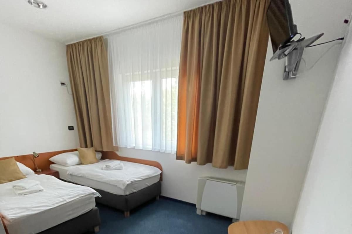A hotel room with two beds, a desk, a chair, a television, and a window with curtains.