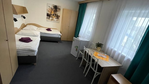 Habitación de hotel con dos camas, un escritorio y una silla. Se puede ver un armario y una ventana con cortinas.