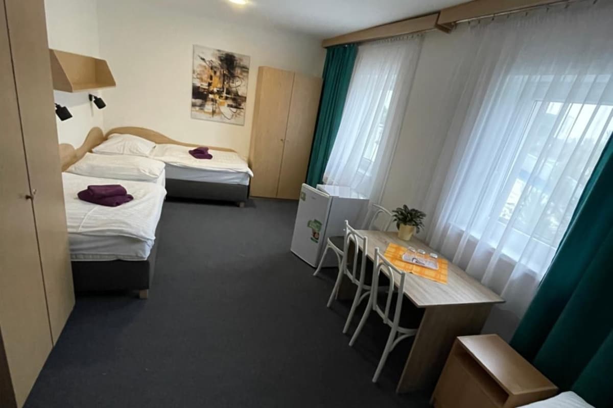 A hotel room with two beds, a desk, and a chair. There is a wardrobe and a window with curtains.