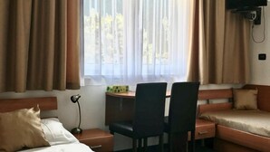 Habitación de hotel con cama, escritorio con dos sillas, televisor y ventana con cortinas.