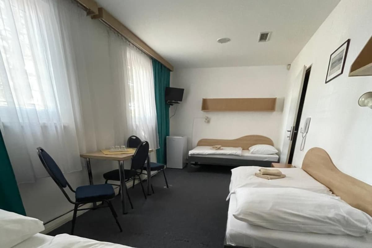 A hotel room with two beds, a desk, a chair, a TV, and a window with curtains.