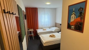 Habitación de hotel con dos camas, una mesita, una silla, un cuadro en la pared y una ventana con cortinas.