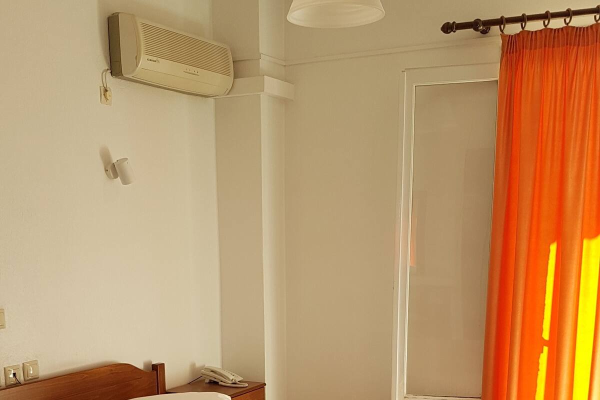 A bedroom with a bed, a bedside table, a lamp, and an air conditioning unit on the wall.