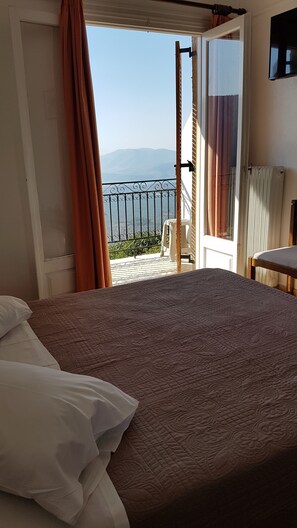 A bedroom with a bed, a view of a balcony, and a chair outside. - Orfeas Hotel (Delphi)