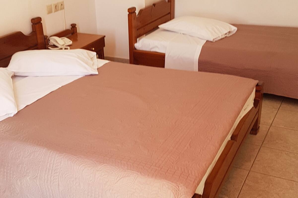 A hotel room with two beds, a wooden headboard, a bedside table with a phone, and a wall socket.