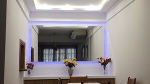 Una habitación con un espejo grande, una lámpara en el techo y dos jarrones con flores sobre una mesa.