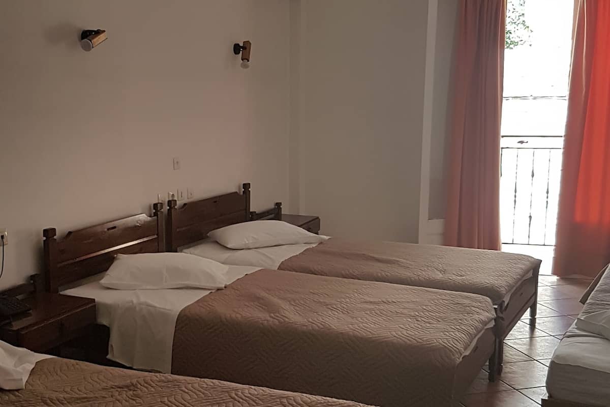 A hotel room with two single beds, a small table, an air conditioning unit, a door with a curtain, and a view of the outside.