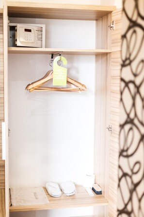 A wooden wardrobe with a hanging space, a microwave on the top shelf, and a pair of slippers and a brush on the bottom shelf.