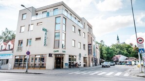 Un hotel de varios pisos con un café y bar en la planta baja, una escalera visible y una vista a la calle con coches y un paso de peatones.