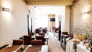 A hotel dining area with multiple tables and chairs, a television screen, and a patterned wall. - Deluxe (Nitra)