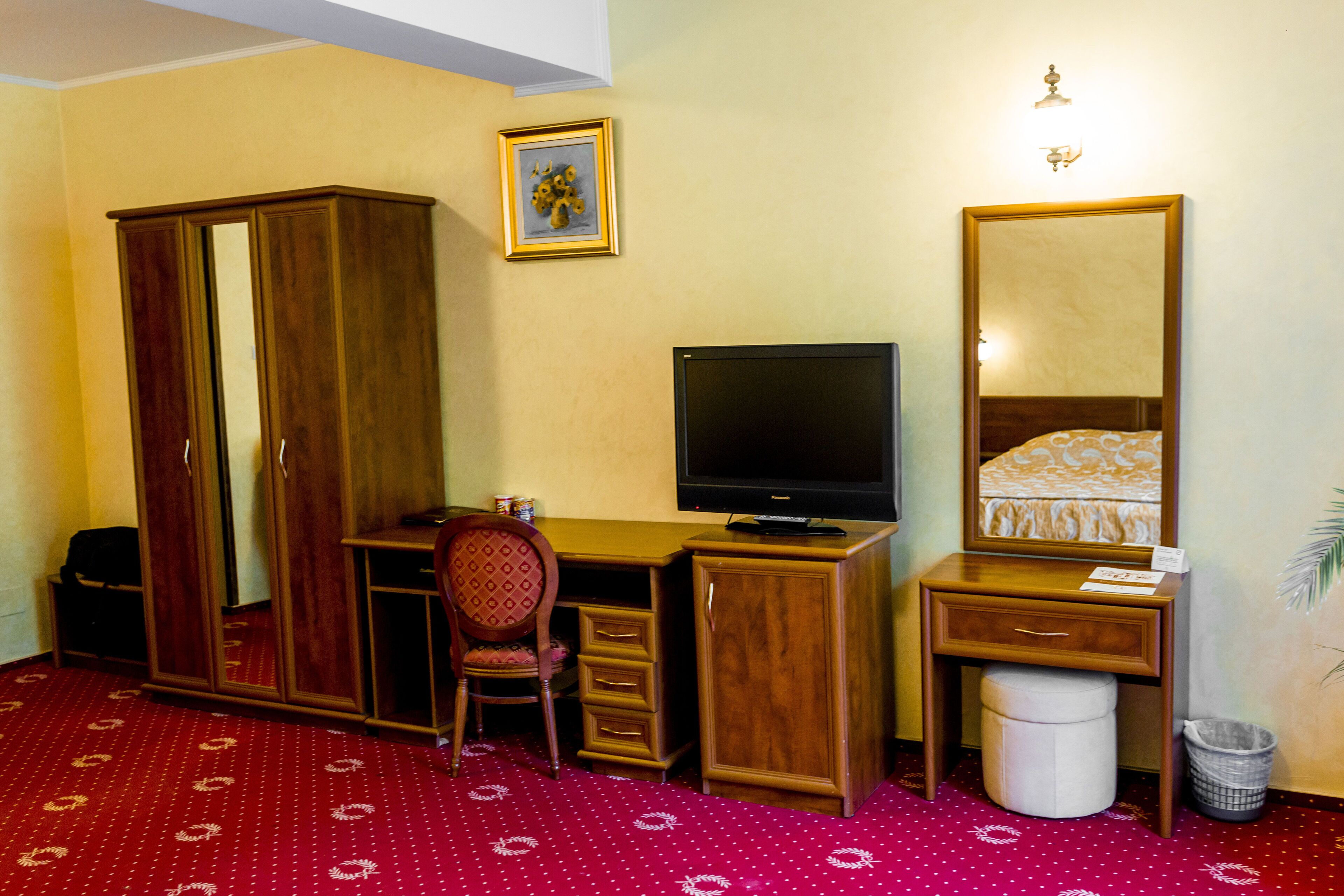 Habitación de hotel con escritorio de madera, televisión, armario, silla y cama con colcha estampada.