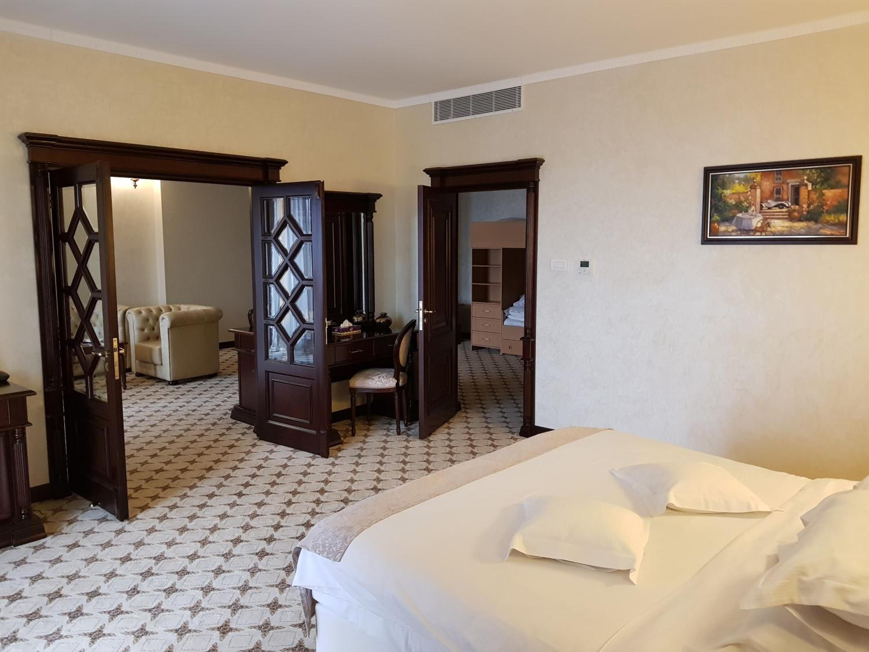 A hotel room with a large bed, a desk with a chair, a wardrobe, and a mirror.