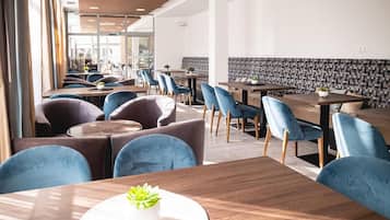 A modern dining area with multiple tables and chairs, a patterned wall, and a view of the outside.