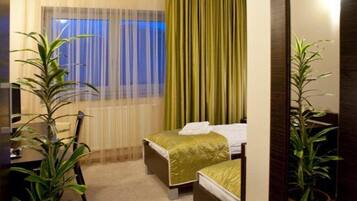 A hotel room with a bed, a desk, and two potted plants.