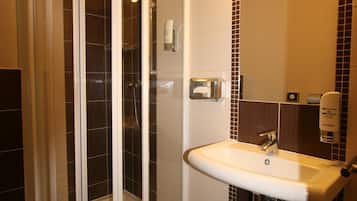 A bathroom with a glass-enclosed shower, a sink with a mirror, and a wall-mounted towel dispenser.