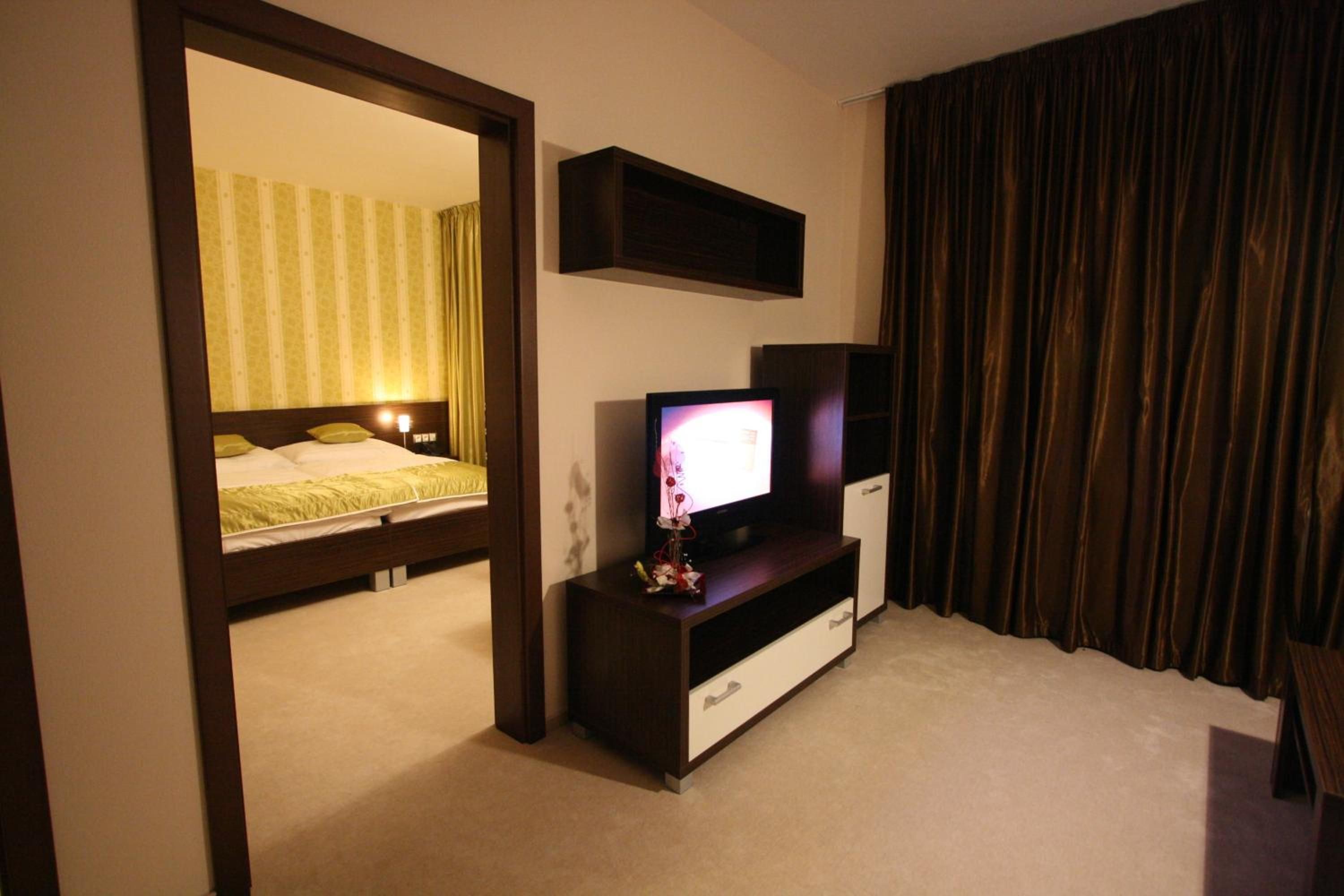 A hotel room with a bed, a TV on a stand, a mirror, and a window with curtains.