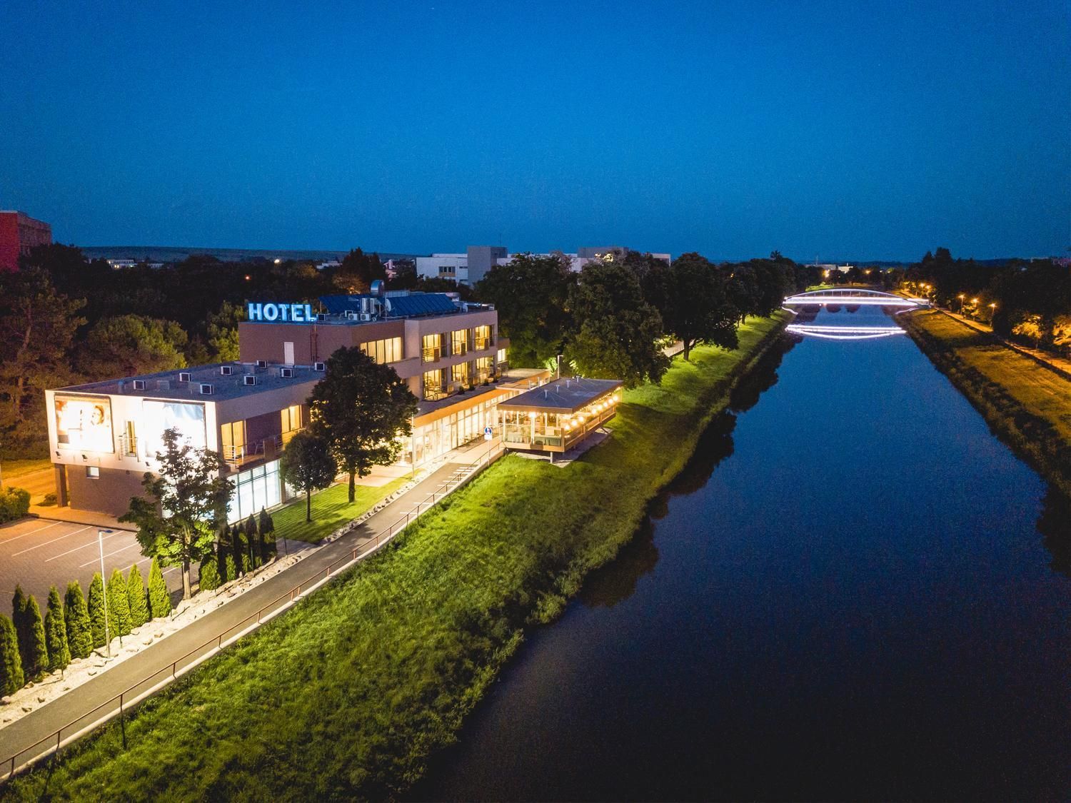 A hotel with a modern design, a parking lot, and a river in the foreground.