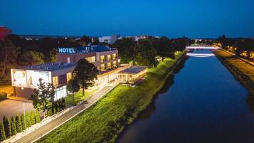 A hotel with a modern design, a parking lot, and a river in the foreground.