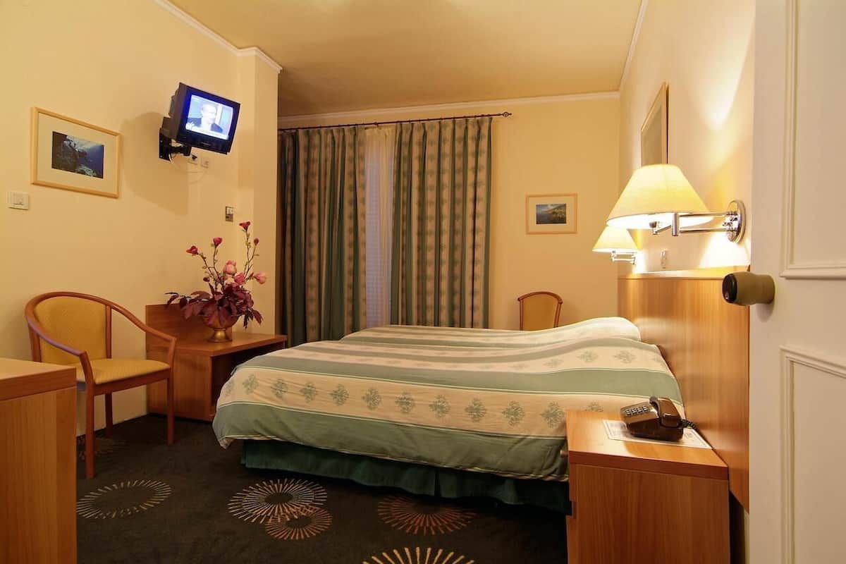 Habitación de hotel con cama, escritorio, silla, televisor montado en la pared, lámpara y teléfono.
