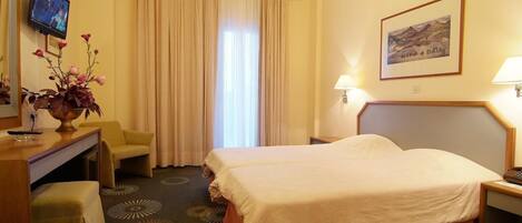 A hotel room with two beds, a desk, a chair, a TV, and a painting on the wall.