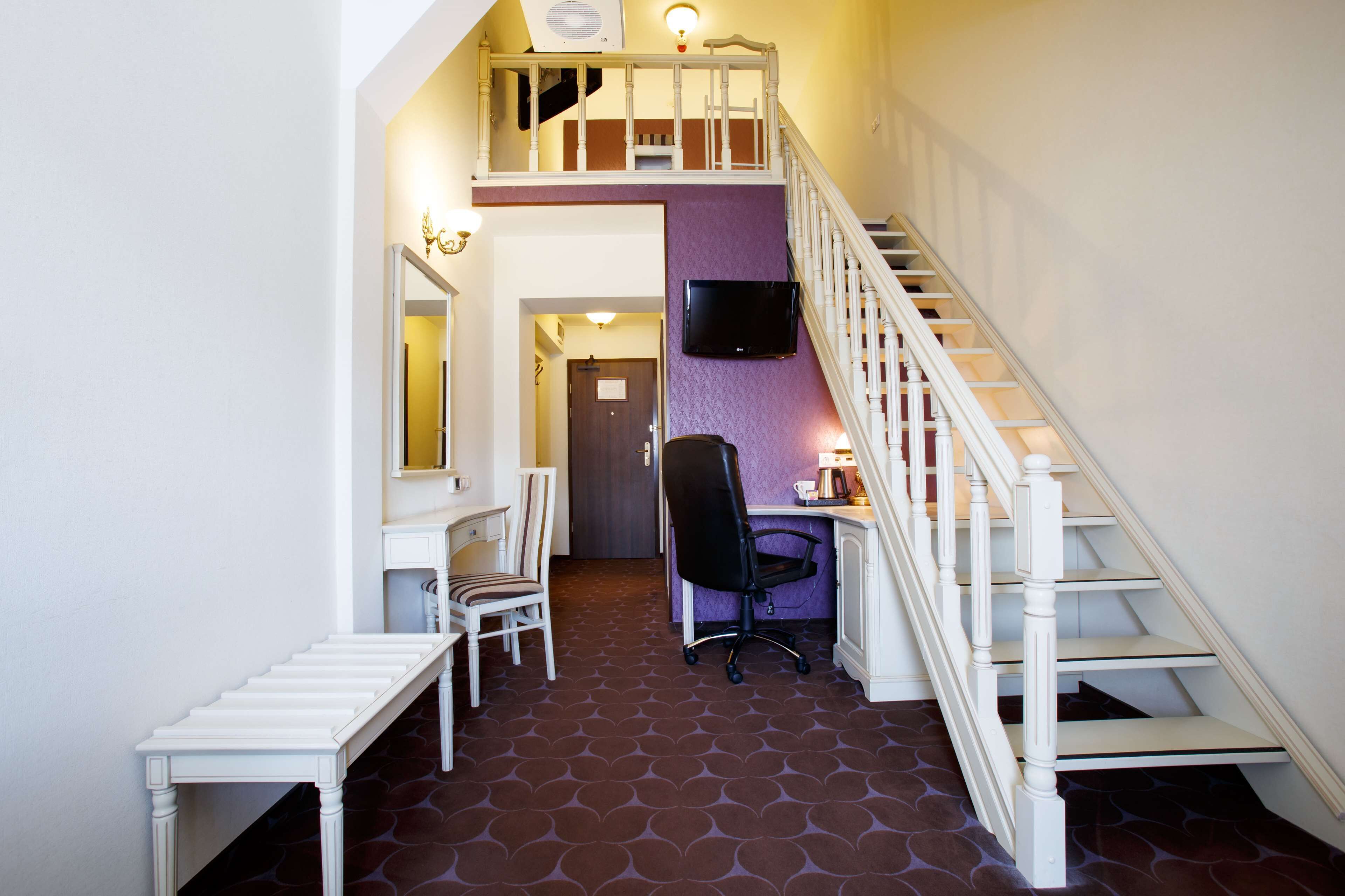A staircase with a white railing leading to a second floor, a desk with a chair, and a television mounted on the wall.