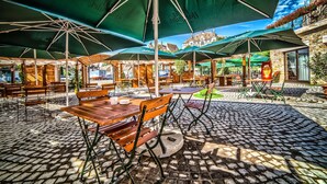 Un café al aire libre con mesas de madera y sombrillas verdes, suelo de adoquines y vista a un edificio histórico al fondo.