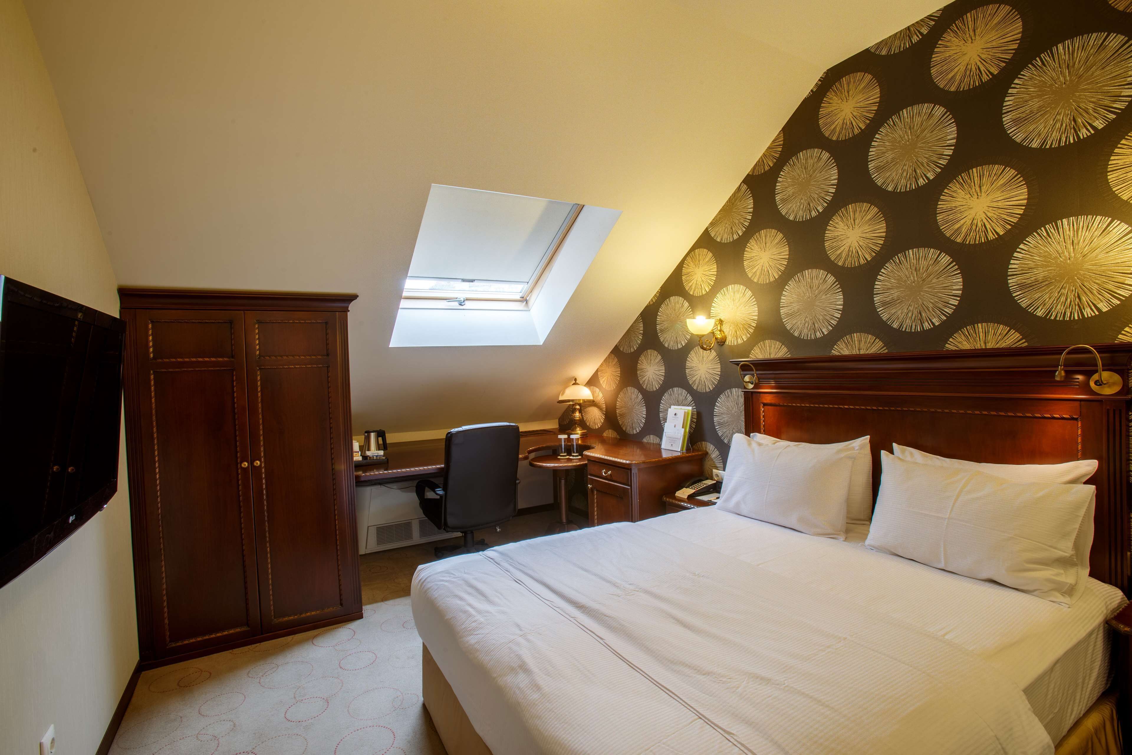 A bedroom with a large bed, a desk, a wardrobe, and a skylight.
