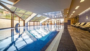 Una piscina interior con tragaluces, un espacio de lounge con camas solarium y vista a un edificio exterior.