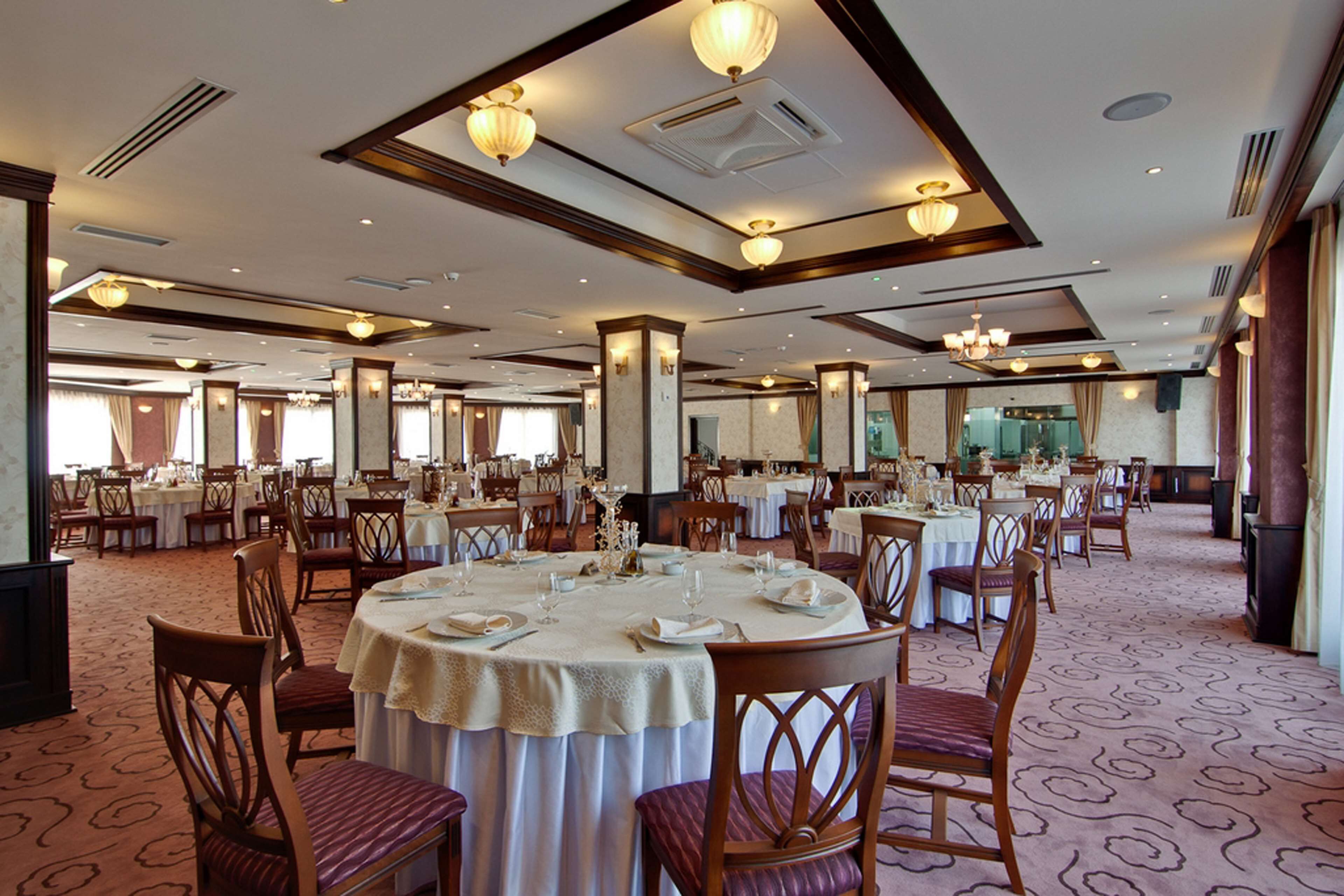 A spacious banquet hall with round tables set for dining, featuring wooden chairs and white tablecloths.