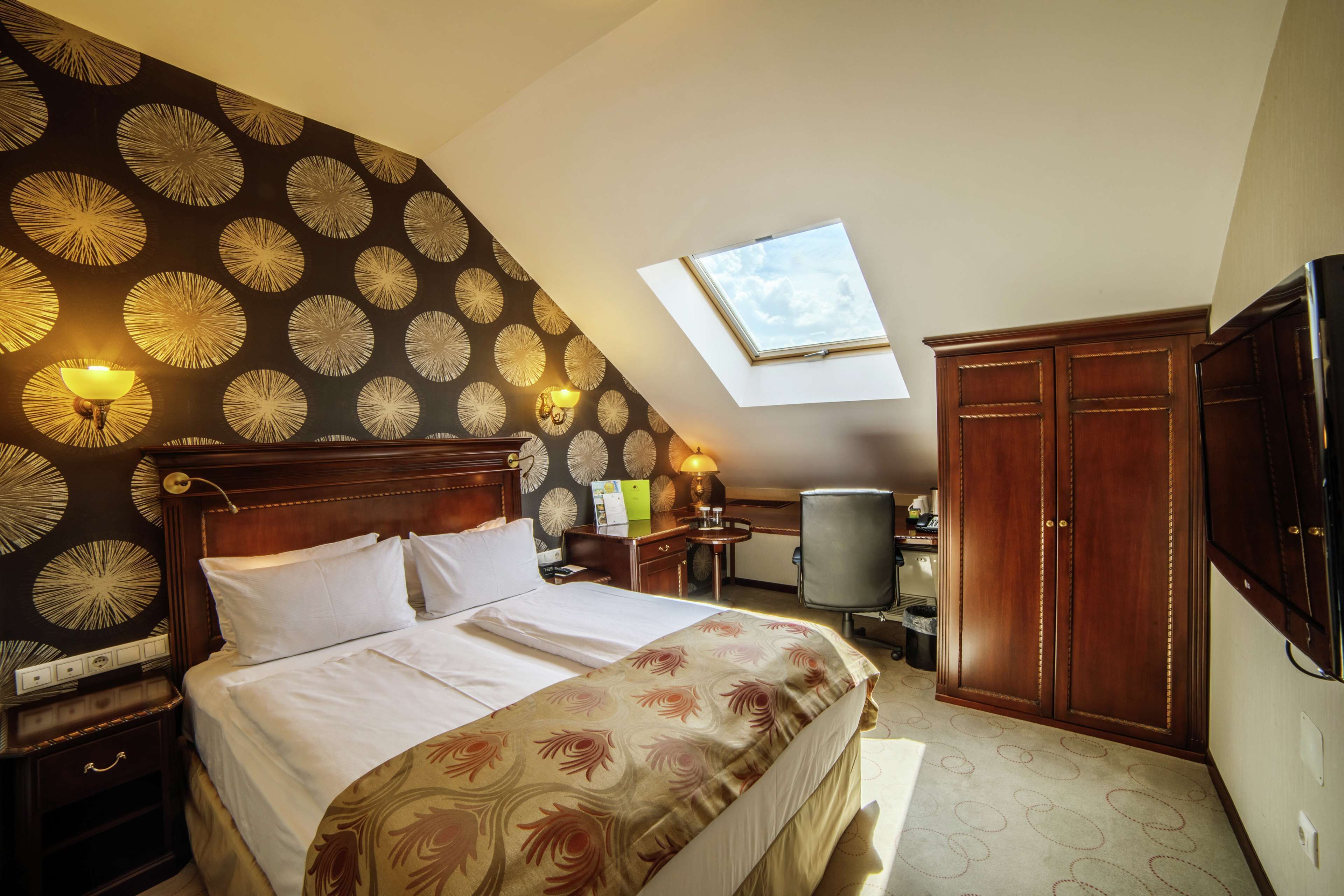 A bedroom with a bed, a desk, a chair, a wardrobe, and a skylight.