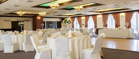 A banquet hall with round tables set for dining, white chairs, and chandeliers.