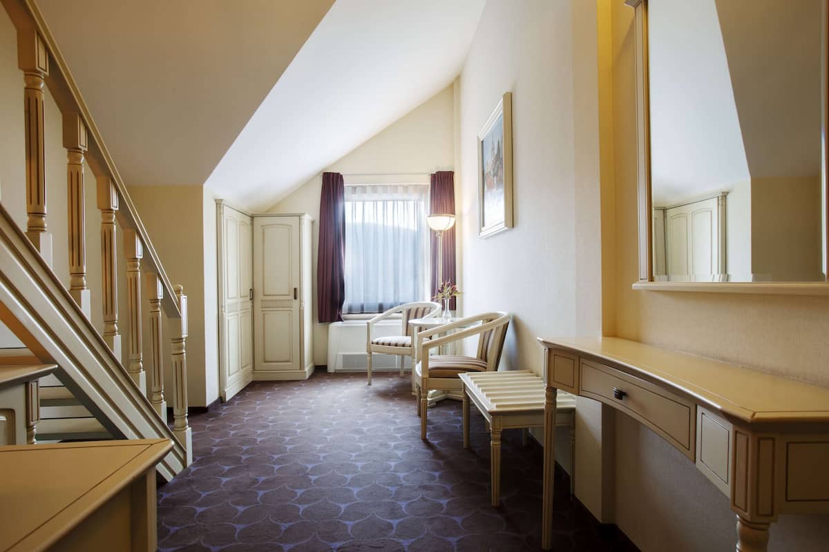 Een hotelkamer met een trap, een bureau, twee stoelen, een raam met gordijnen en een spiegel aan de muur.