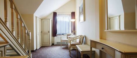A hotel room with a staircase, a desk, two chairs, a window with curtains, and a mirror on the wall.