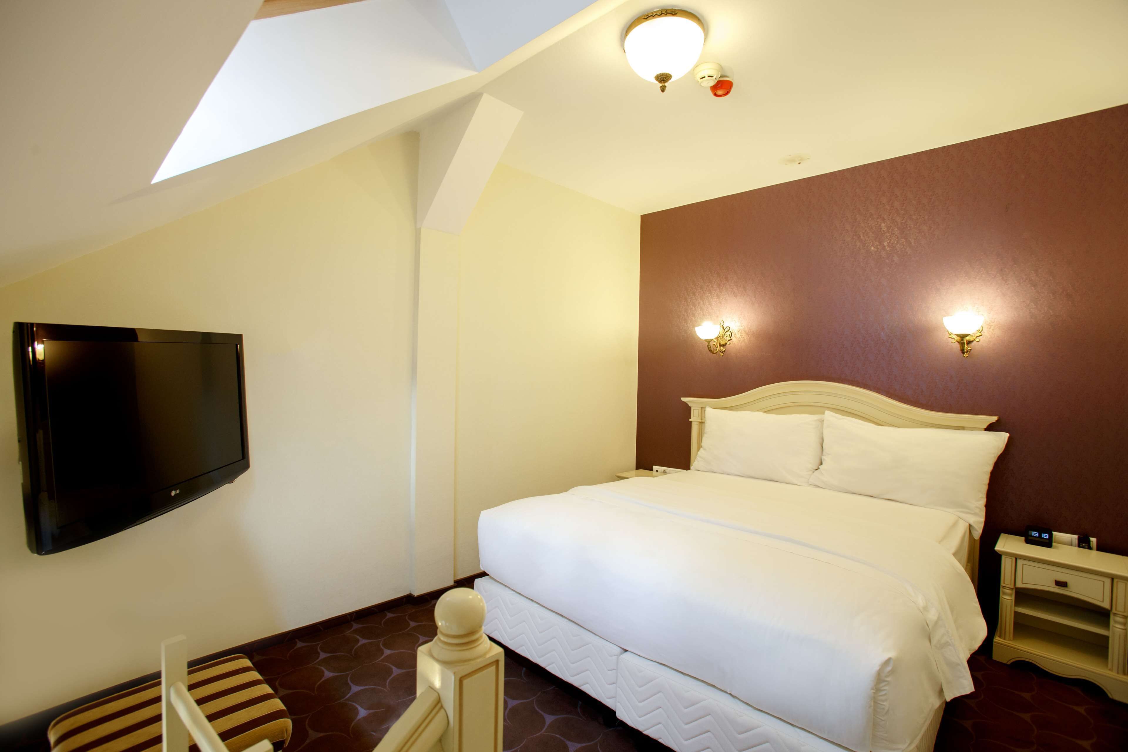 Una habitación de hotel con una cama, televisor montado en la pared y una mesita de noche con lámpara.