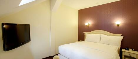 Una habitación de hotel con una cama, televisor montado en la pared y una mesita de noche con lámpara.