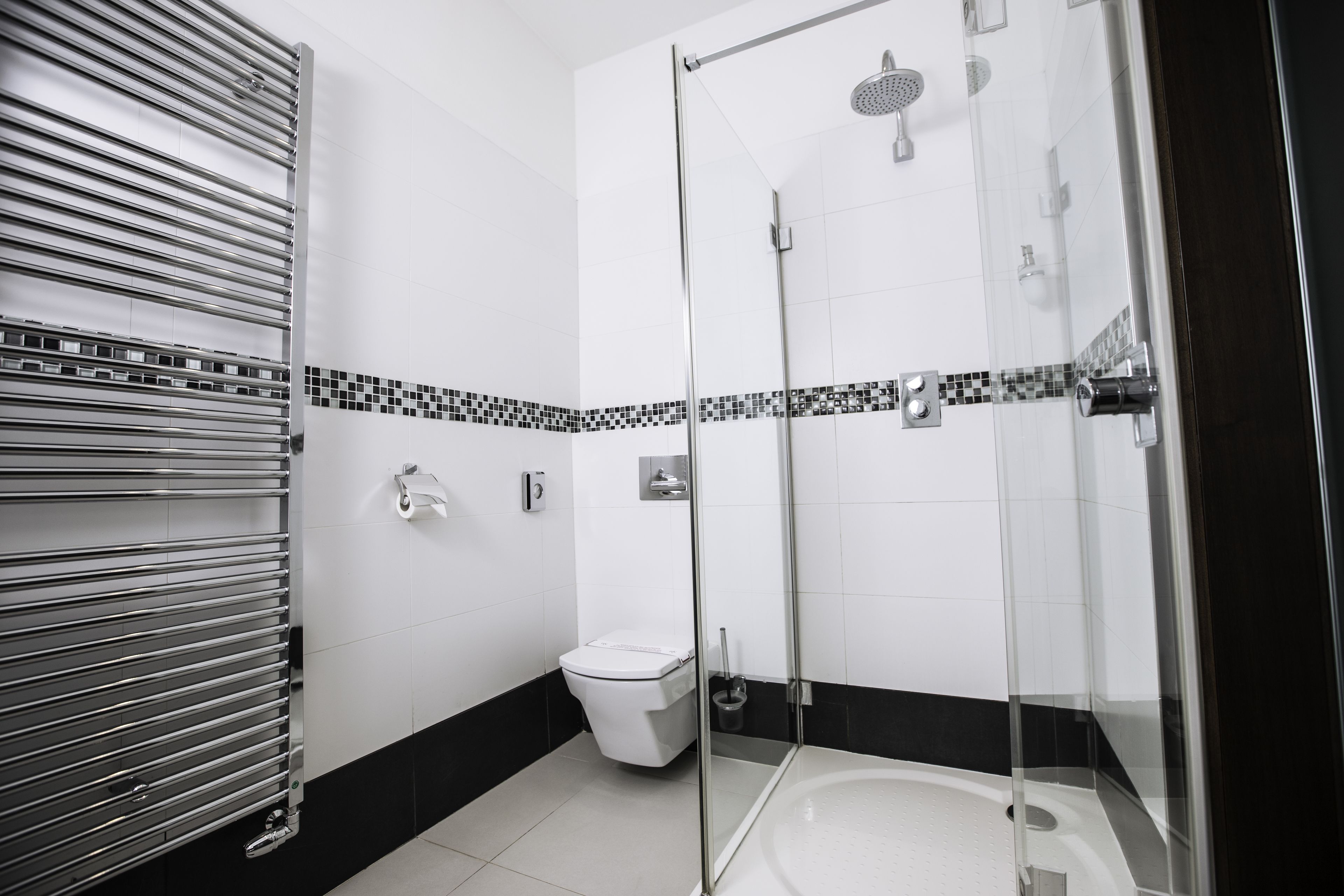 Et moderne badeværelse med et glasafskærmet brusebad, toilet og håndklædetørre.