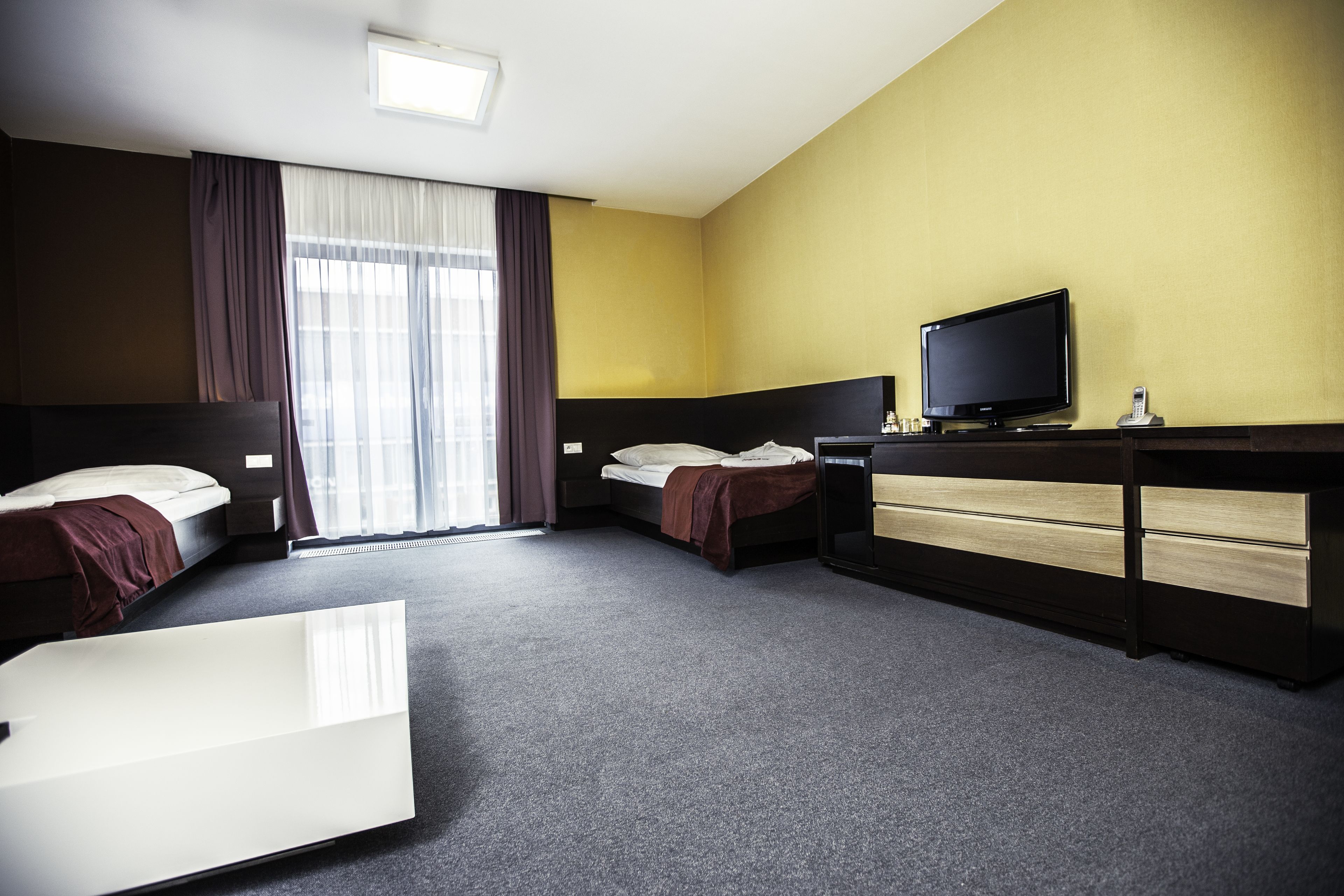 Une chambre d’hôtel avec deux lits, un bureau avec une télévision et une grande fenêtre avec des rideaux.