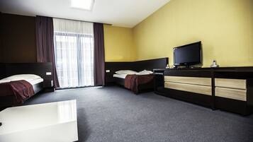 Une chambre d’hôtel avec deux lits, un bureau avec une télévision et une grande fenêtre avec des rideaux.