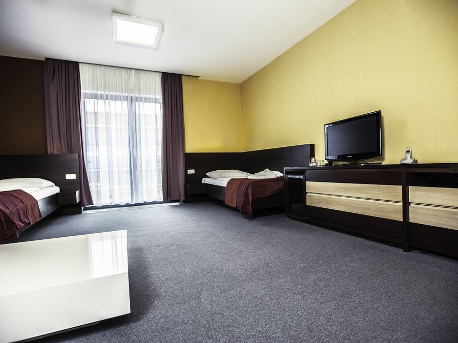 Une chambre d’hôtel avec deux lits, un bureau avec une télévision et une grande fenêtre avec des rideaux.
