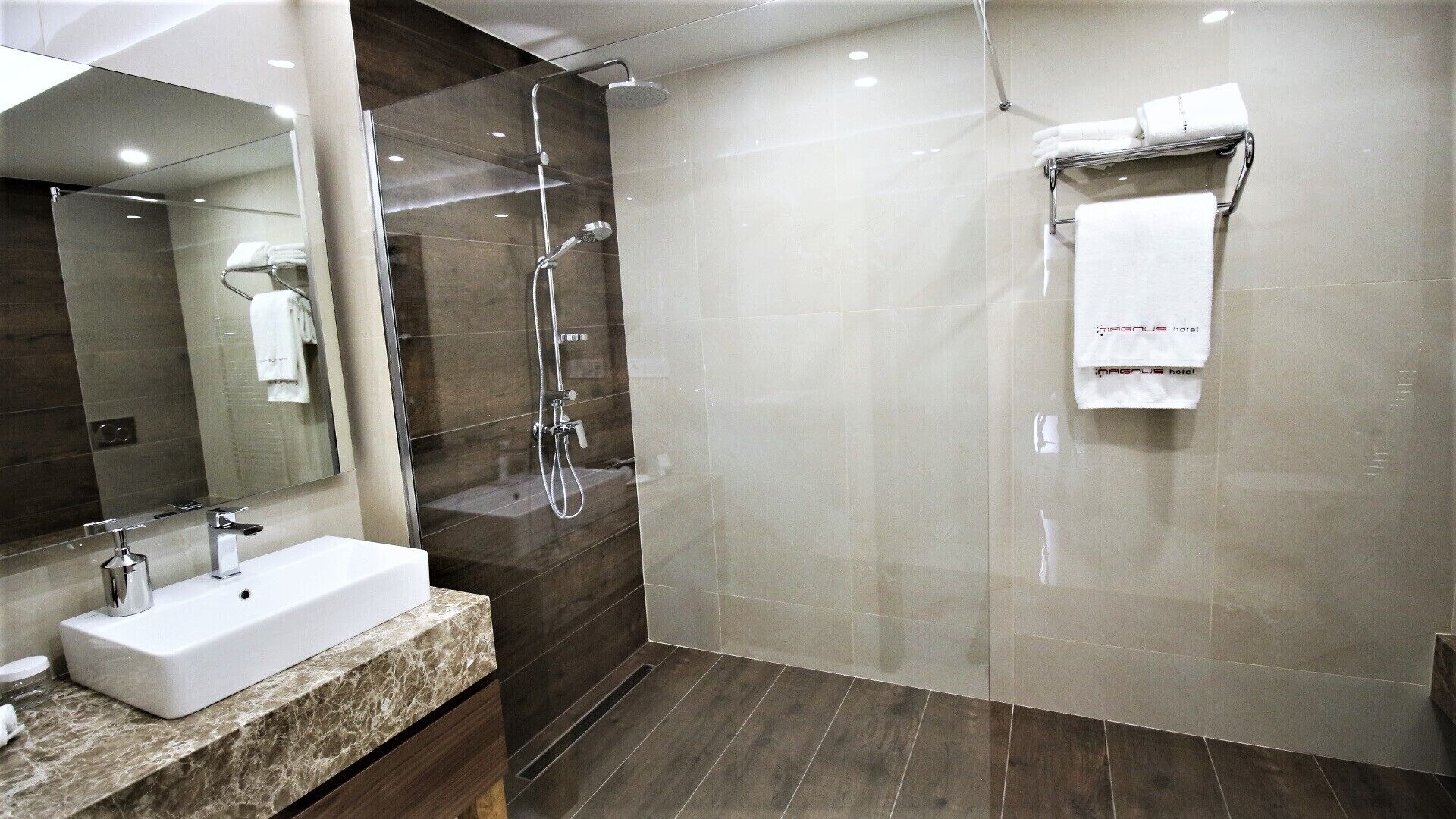 Un baño moderno con ducha envuelta en vidrio, encimera de mármol y un espejo grande.