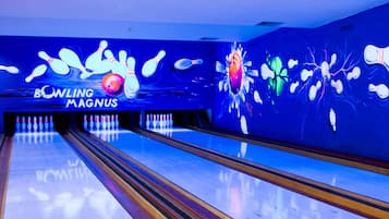 A bowling alley with multiple lanes, a neon sign reading "BOWLING MAGNUS," and a colorful mural on the wall.