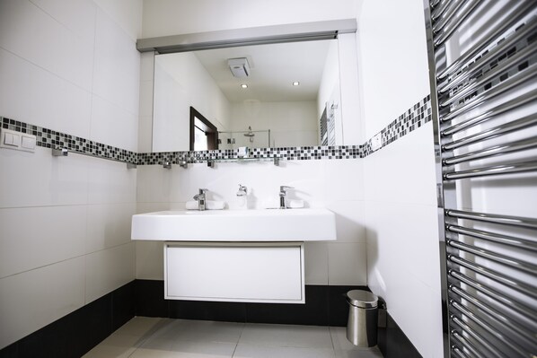 Un baño moderno con lavamanos blanco, salpicadero de azulejos blanco y negro y radiador de acero inoxidable.