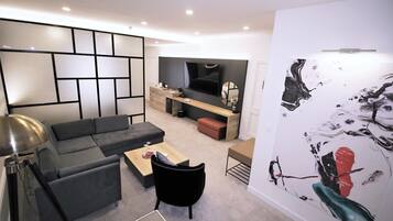 Un salon moderne avec un canapé d’angle, une table basse et un fauteuil noir. Un téléviseur est fixé au mur, ainsi qu’un meuble en bois et un grand tableau abstrait.