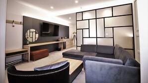 Un salon moderne avec un canapé, un pouf et un téléviseur fixé au mur.